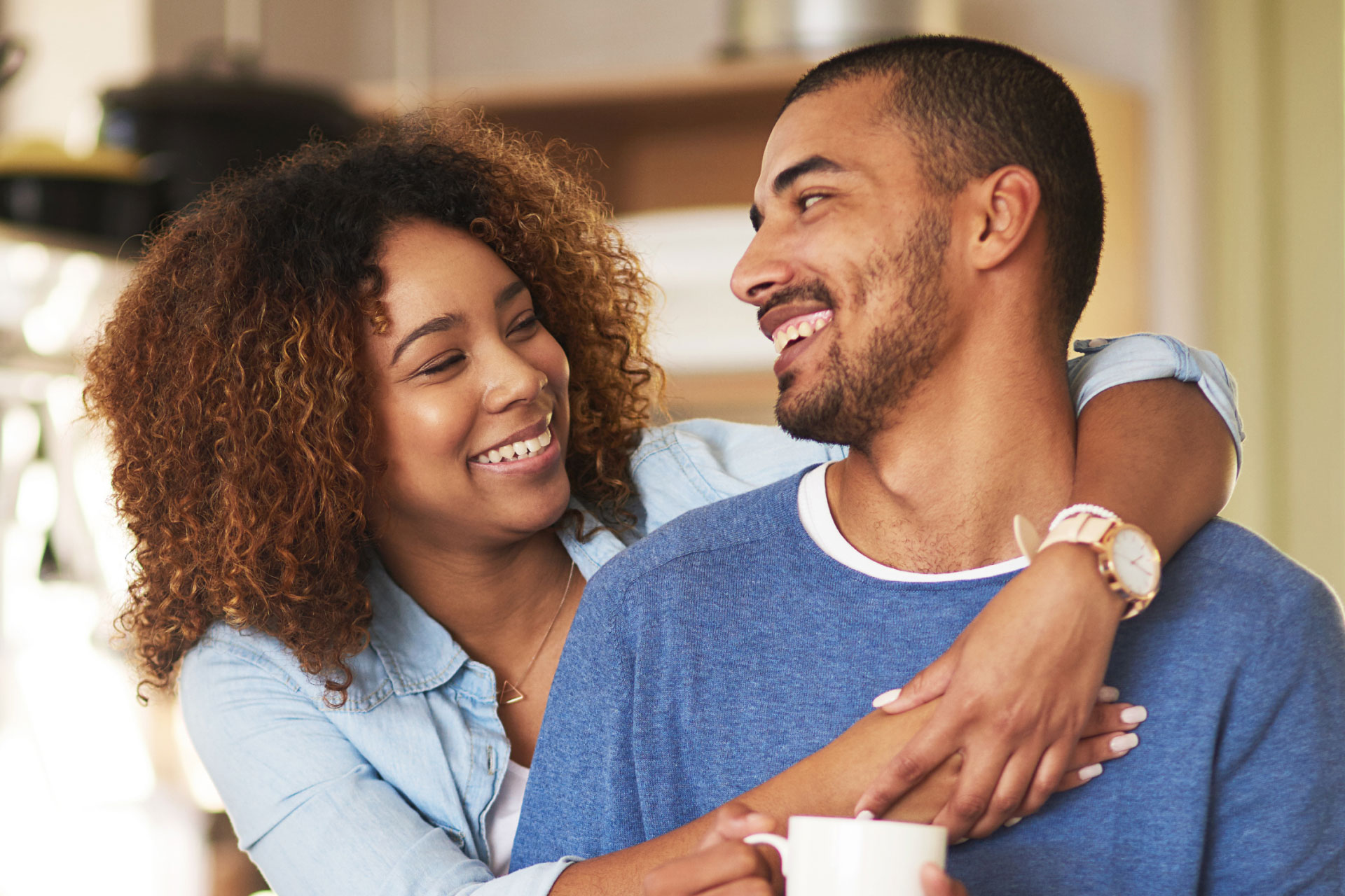 young african american couple hugging and smiling at each other at home